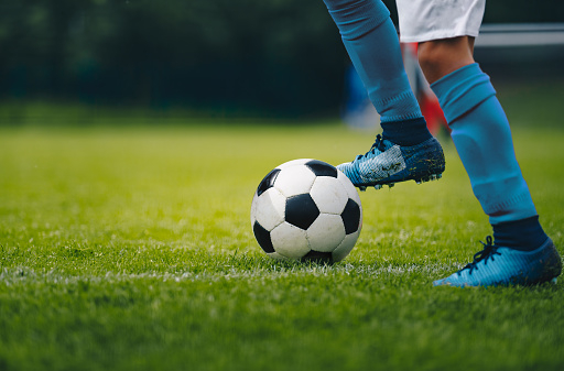 Close up of legs and feet of football player in blue socks and shoes running and dribbling with the ball. Soccer player running after the ball. Sports venue in the background