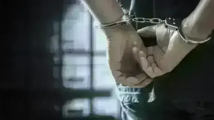 Arrested man in handcuffs with handcuffed hands behind back in prison